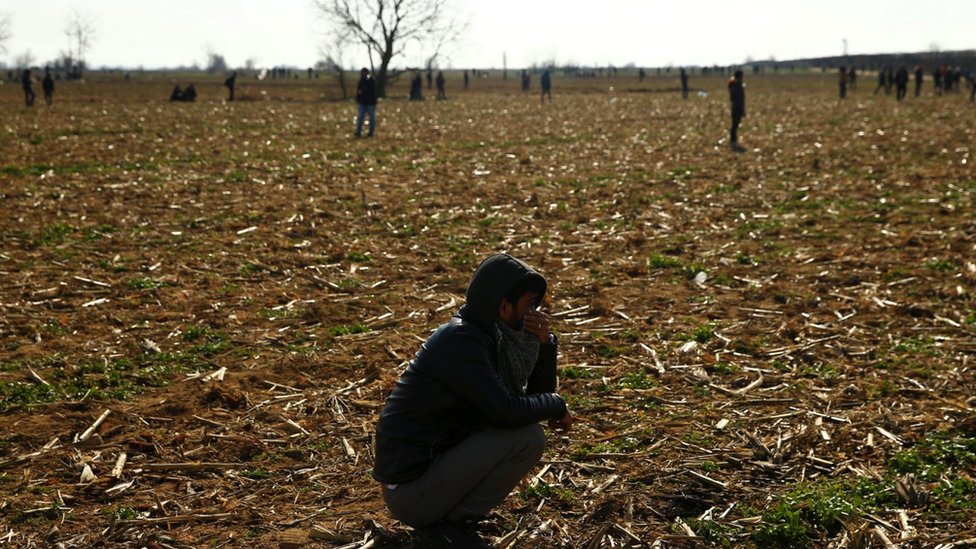 A migrant covers his face, crouching in a field, as others make their way towards the Pazarkule crossing at the Turkish-Greek border in Turkey on 2 Mar 2020