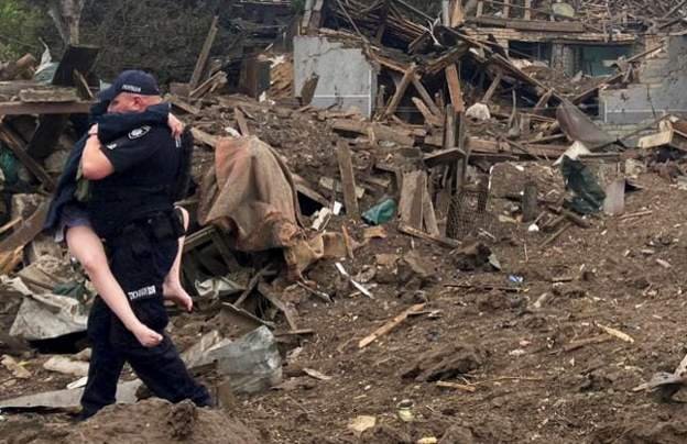 Policajac nosi dete iz uništene kuće u Kramatorsku