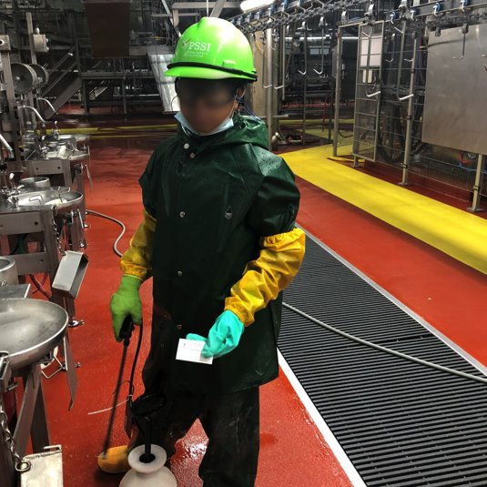 A child wearing protective clothing cleans equipment in a slaughterhouse