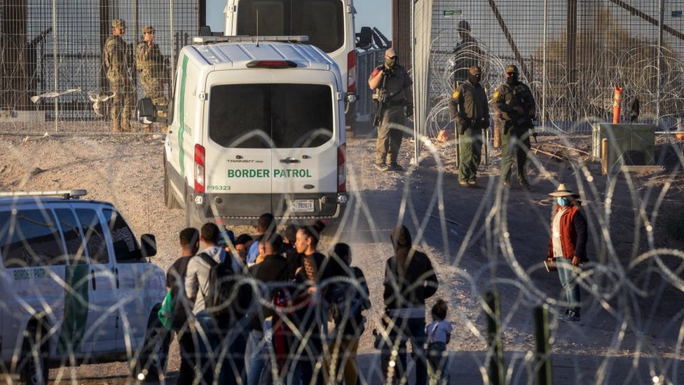 Border patrol officers and migrants at a heavily fortified border