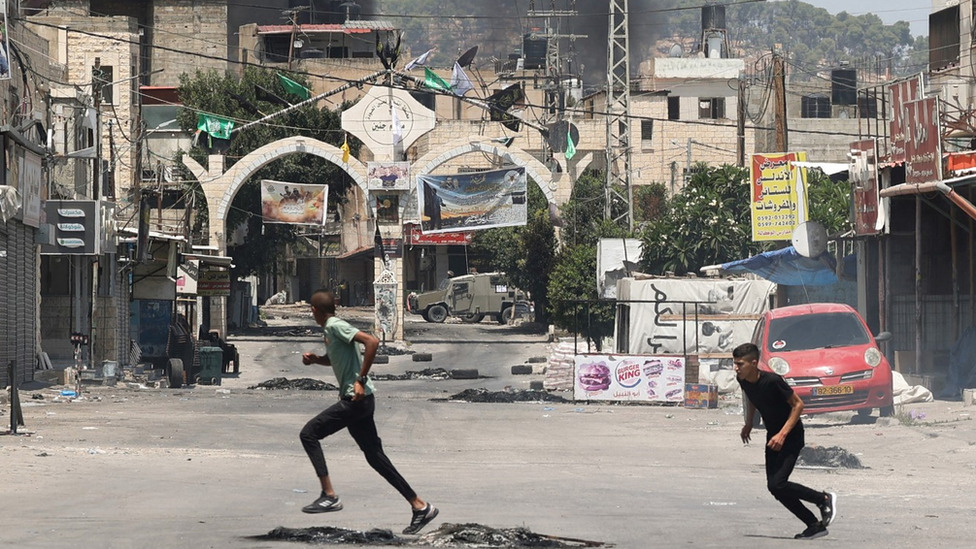 Youths run across the road outside the entrance to Jenin refugee camp.