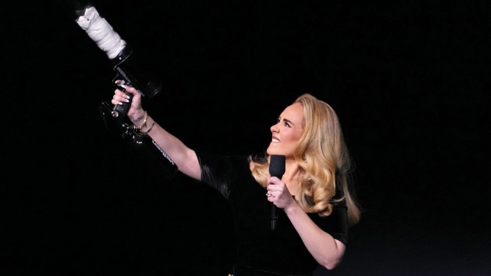 Adele on stage holding a T-shirt thrower in one hand and a microphone in the other
