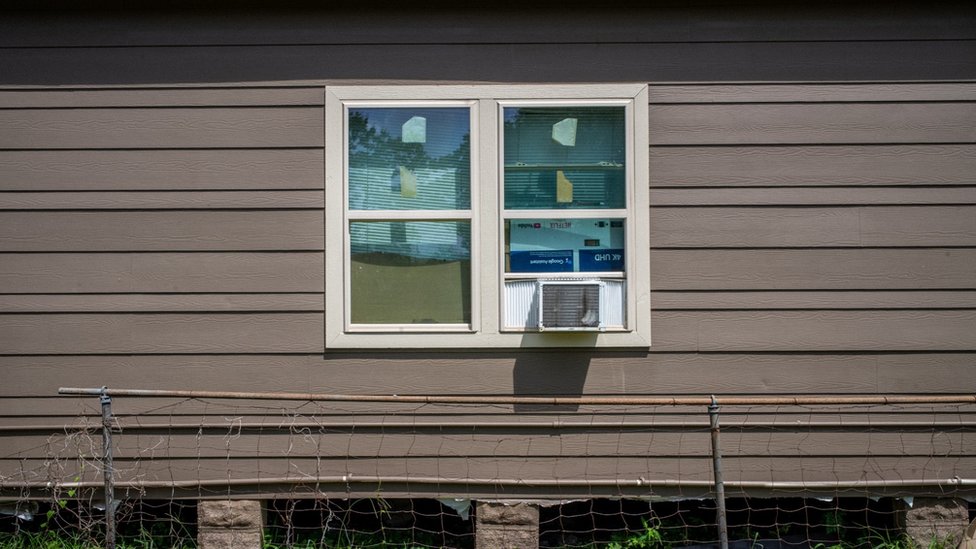 A house with windows boarded by cardboard and with an air conditioning unit
