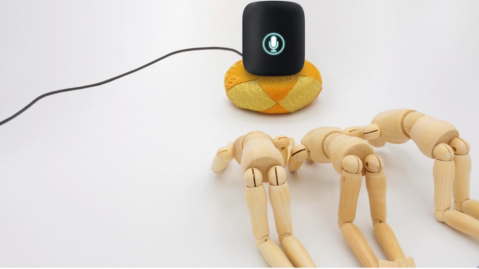 Artistic image shows wooden figures worshiping an AI speakers