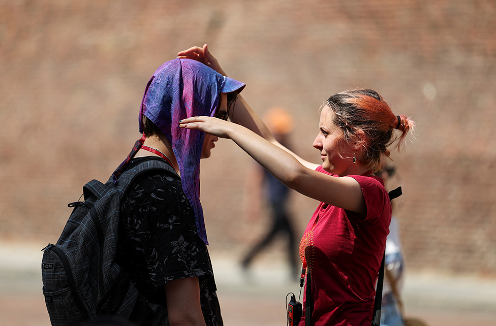 A woman puts a wet scarf on a man to protect him from the sun in Bologna, Italy