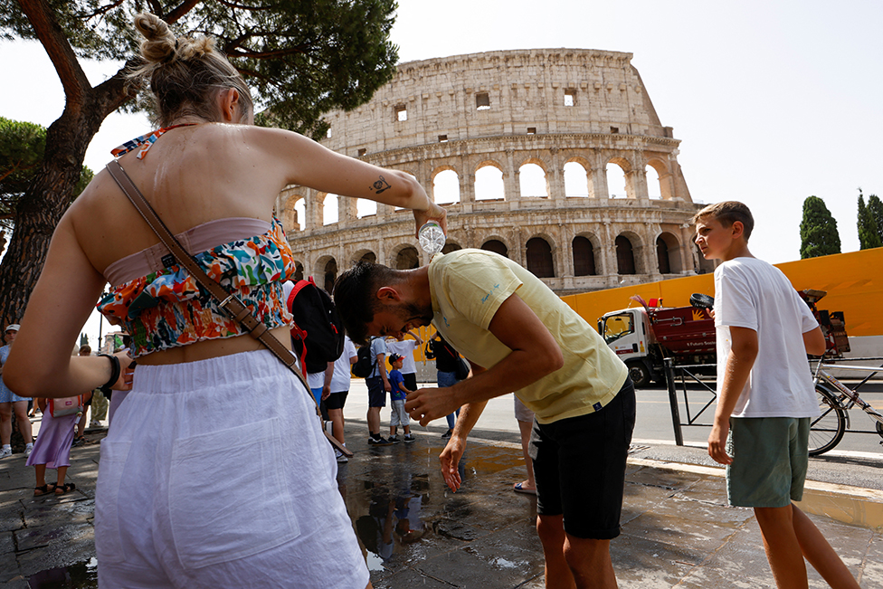 A woman pours water on a man near the Colosseum in Rome, Italy