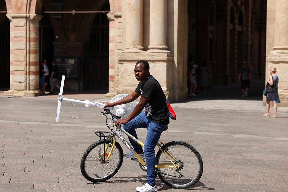 Toplotni talas ’Kerber’: Crveni meteoalarm u skoro celoj Italiji, u Grčkoj besne požari, prognozira se pad temperature od četvrtka 8 A man carries an electric fan with a bike in Bologna, Italy