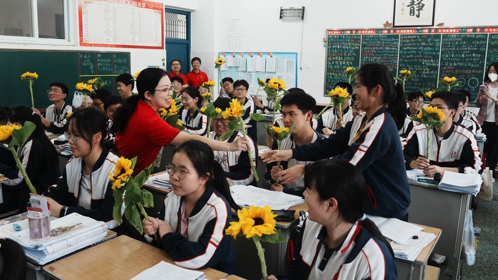 A teacher distributes sunflowers to her students to cheer up for them ahead of the 2023 National College Entrance Exam (Gaokao) at a classroom of a high school on 1 June, 2023 in Luoyang, Henan Province of China.