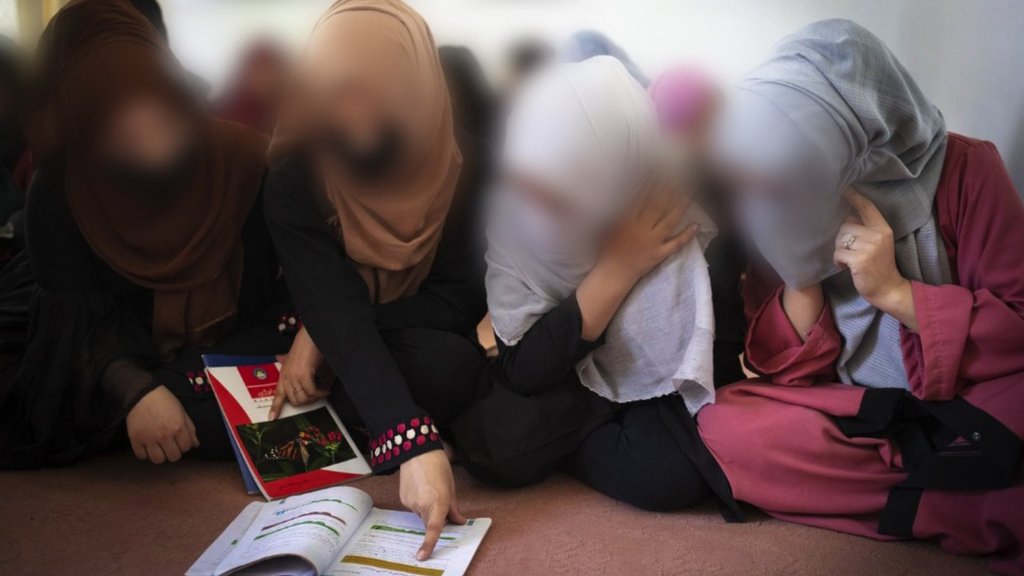 Young Afghan women gather around a shared textbook in a small classroom