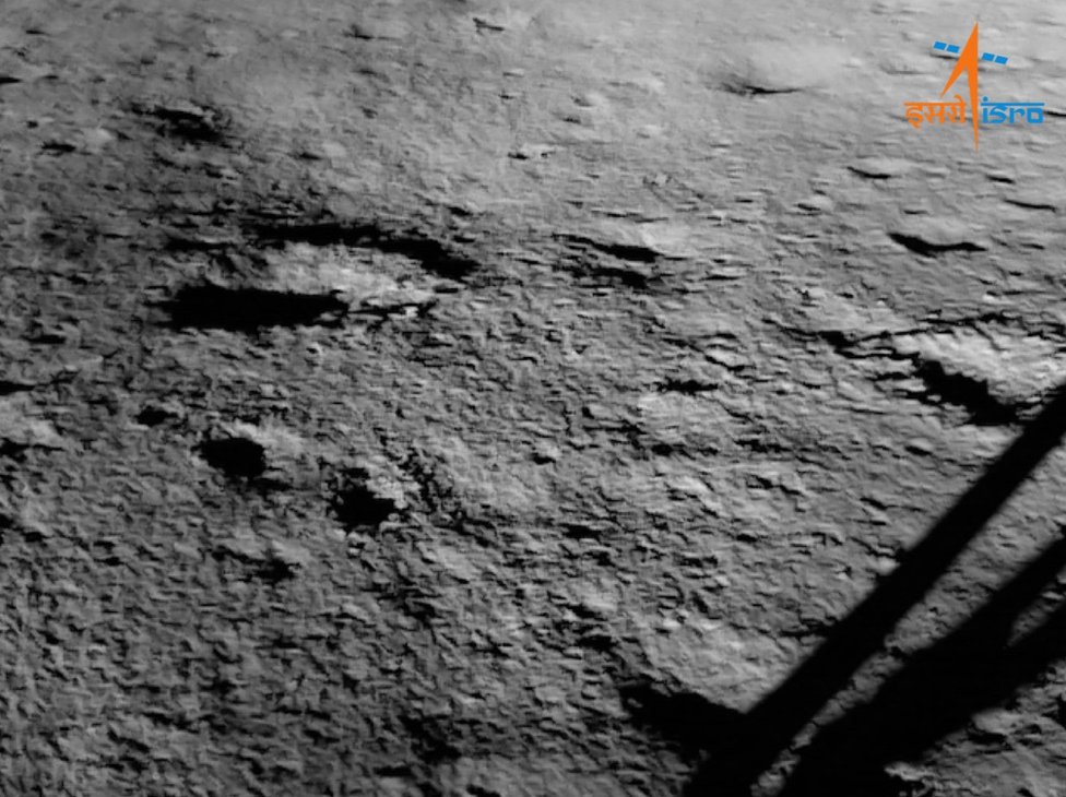 Čandrajan-3: Indijski lunarni rover Pragjan se provozao Mesecom 1 An Isro image of the Chandrayaan-3 landing site taken after touchdown. One of the four legs of the lander is visible on the right