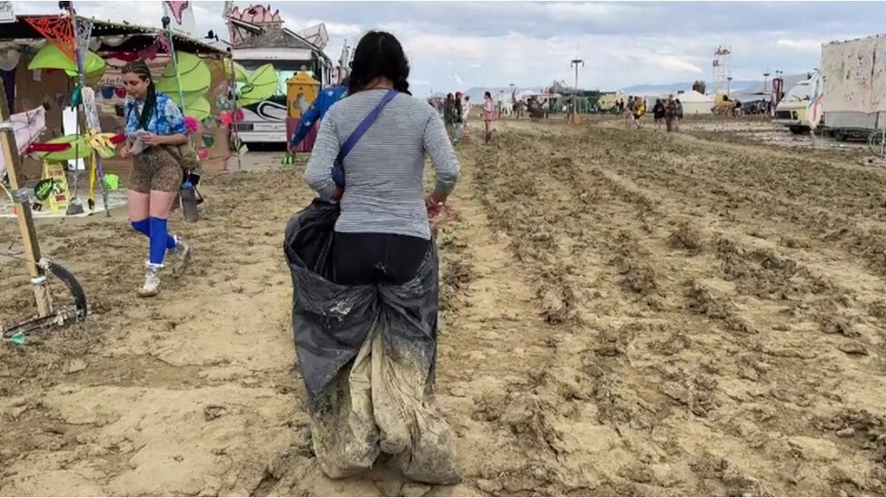 A woman walks through mud using a bin bag at Burning Man in Nevada