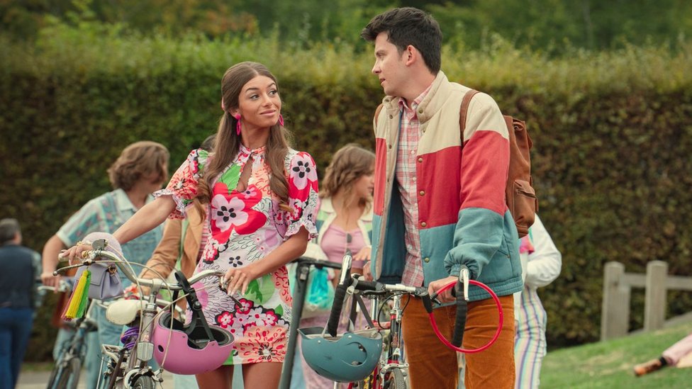 „Seksualno obrazovanje“: Autorka Lori Nan ponosna je na uticaj serije i razbijanje tabua 1 Mimi Keene as Ruby and Asa Butterfield as Otis in Sex Education. Ruby and Otis are speaking to each other outside as they wheel their bikes. Ruby, a young woman with long light brown hair, wears a short floral dress and large pink earrings. Otis, a young man with short dark hair, wears orange cord trousers, a pink plaid shirt and a blue, cream and red striped puffer jacket.