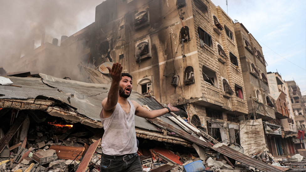 A man reacts outside a burning collapsed building following Israeli bombardment in Gaza City on 11 October 2023