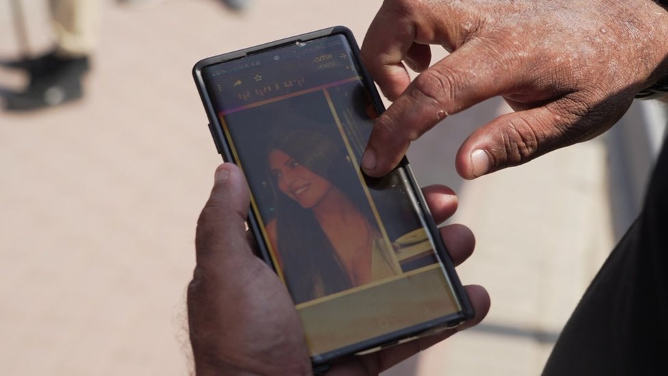 Israel holds a phone showing a picture of his daughter, Kim