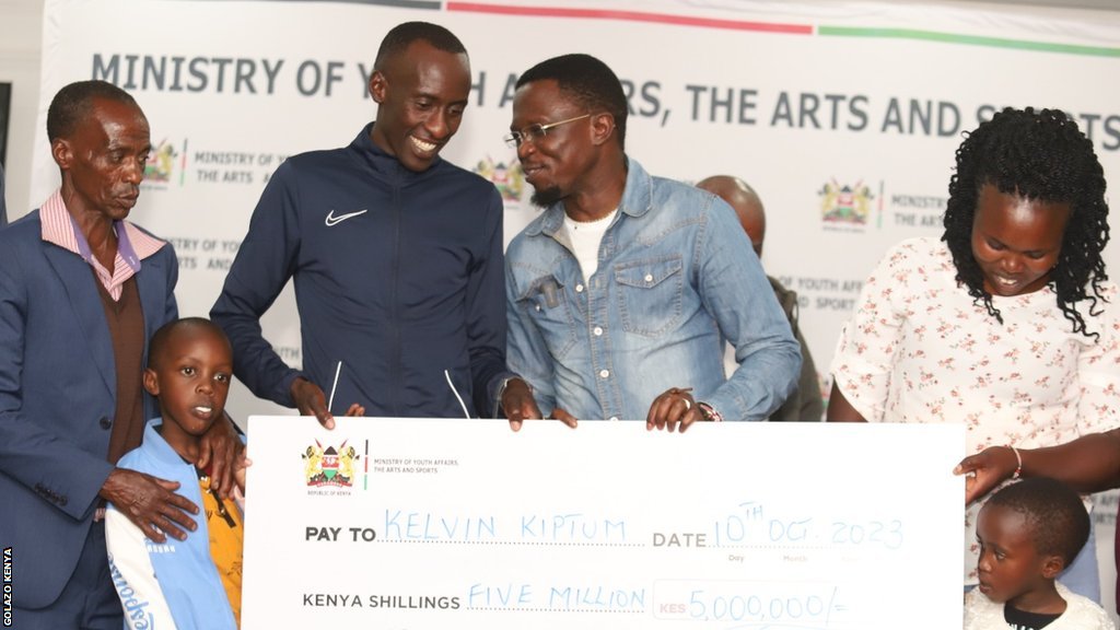 Kelvin Kiptum i maraton: Od pozajmljenih patika do obaranja svetskih rekorda 3 Runner and marathon world record holder Kelvin Kiptum's father, wife and children joined him to accept his government award from Kenya's sports minister