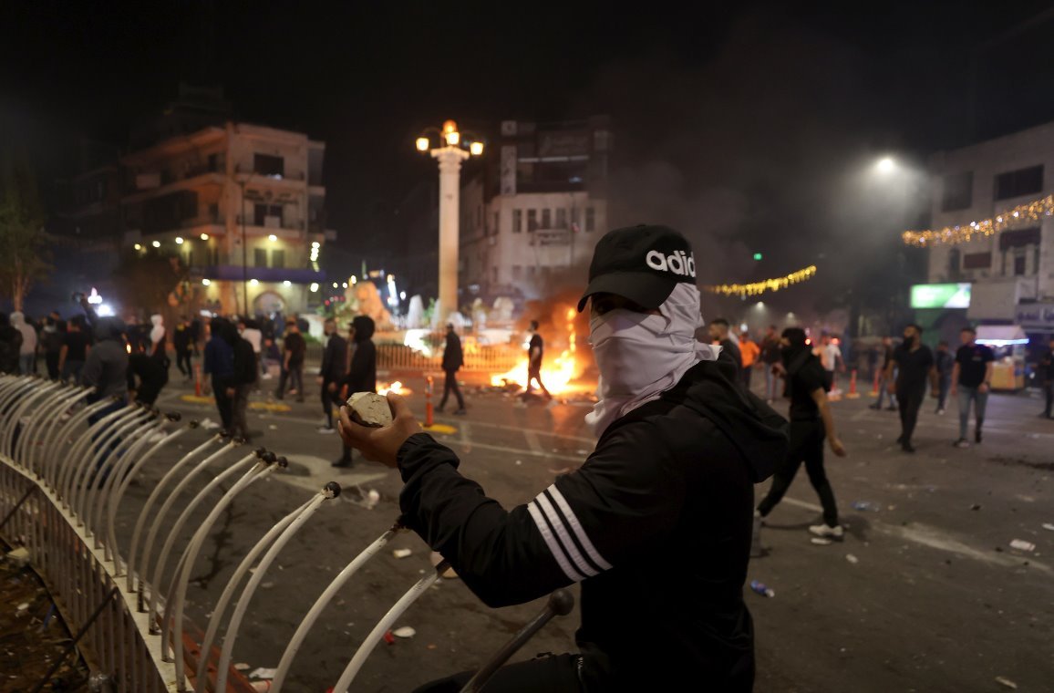 Masked protester holding rocks in front of a barricade and fires