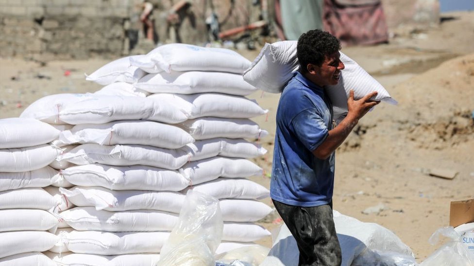 Izrael i Palestinci: Kakva pomoć je potrebna ljudima u Gazi 1 A Palestinian man carries a bag of flour provided as aid to families at the United Nations Relief and Works Agency for Palestine Refugees (UNRWA) distribution centre, in the Al-Shati refugee camp in Gaza city on 31 July 2023