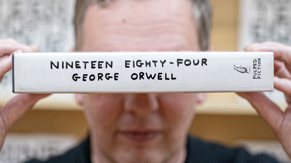 Umetnik Dejvid Šrigli drži kopiju Džordža Orvela iz 1984. preko očiju.