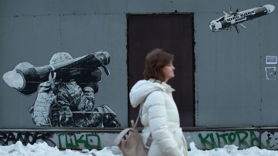 Një grua ecën përpara grafitit që përshkruan një ushtarak ukrainas duke bërë një goditje me një antitank portativ Javelin të prodhuar në SHBA