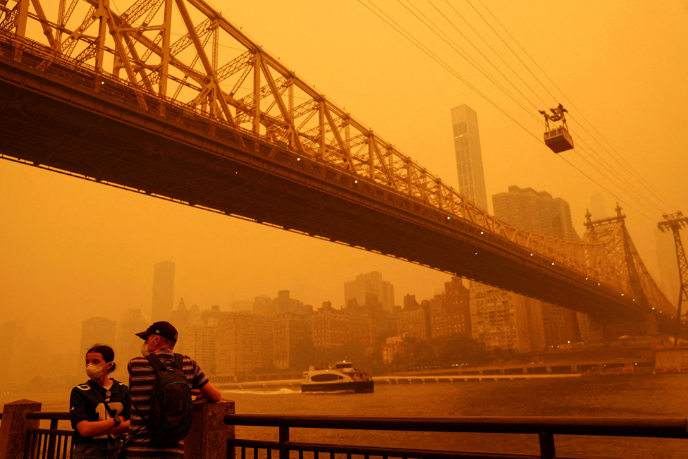 People wear protective masks as the Roosevelt Island Tram crosses the East River while haze and smoke from the Canadian wildfires shroud the Manhattan skyline in the Queens Borough New York City, U.S., June 7, 2023.
