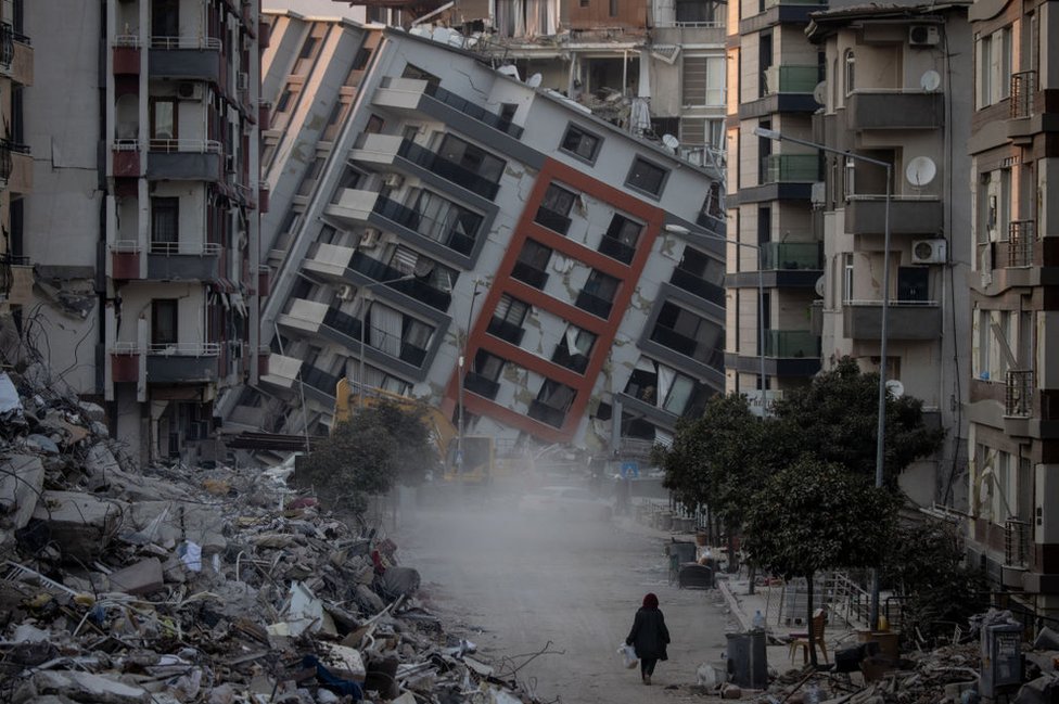 A woman walks on a street amid destroyed buildings on February 17, 2023 in Hatay, Turkey.