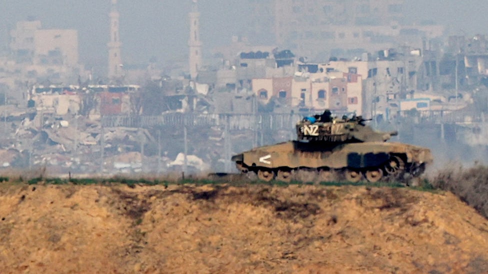 An Israeli tank is seen on a ridge with the skyline of southern Gaza in the background. Image taken from Israel side of border on 7 December.
