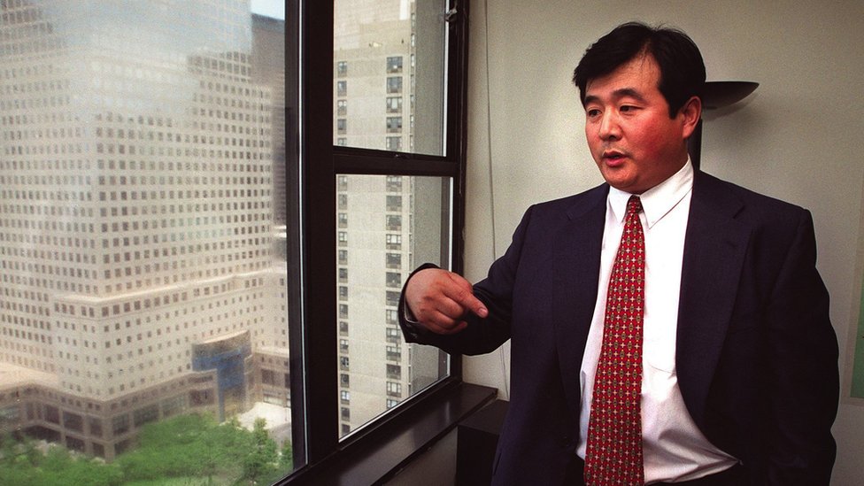 Falun Gong: Zabranjena kineska sekta koja raste van Kine 4 Li Hong Zhi stands gesticulating in a business suit in an office overlooking other large buildings