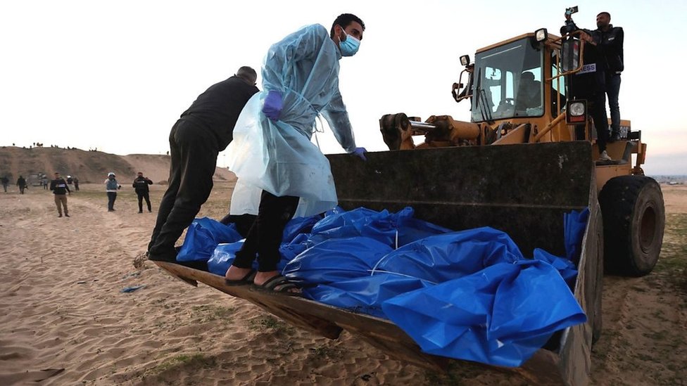 Bulldozer carrying bodies in blue bags