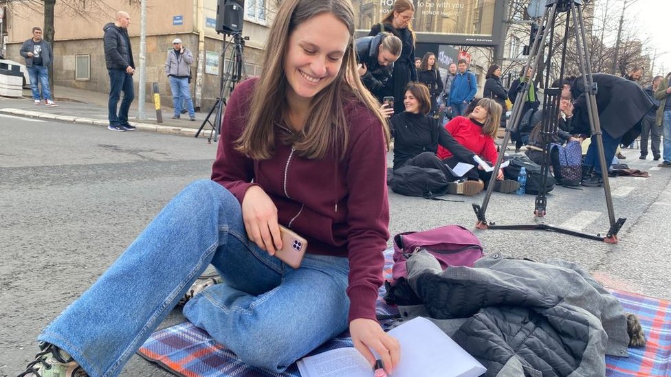 devojka sedi na ulici sa otvorenom knjigom