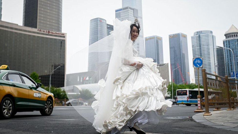 Kina: Kako Komunistička partija učestvuje u provodadžisanju 1 A woman crosses a road before posing for wedding photos in Beijing on May 5, 2023.
