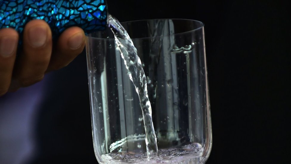 Water is poured into a glass from an elaborately decorated bottle