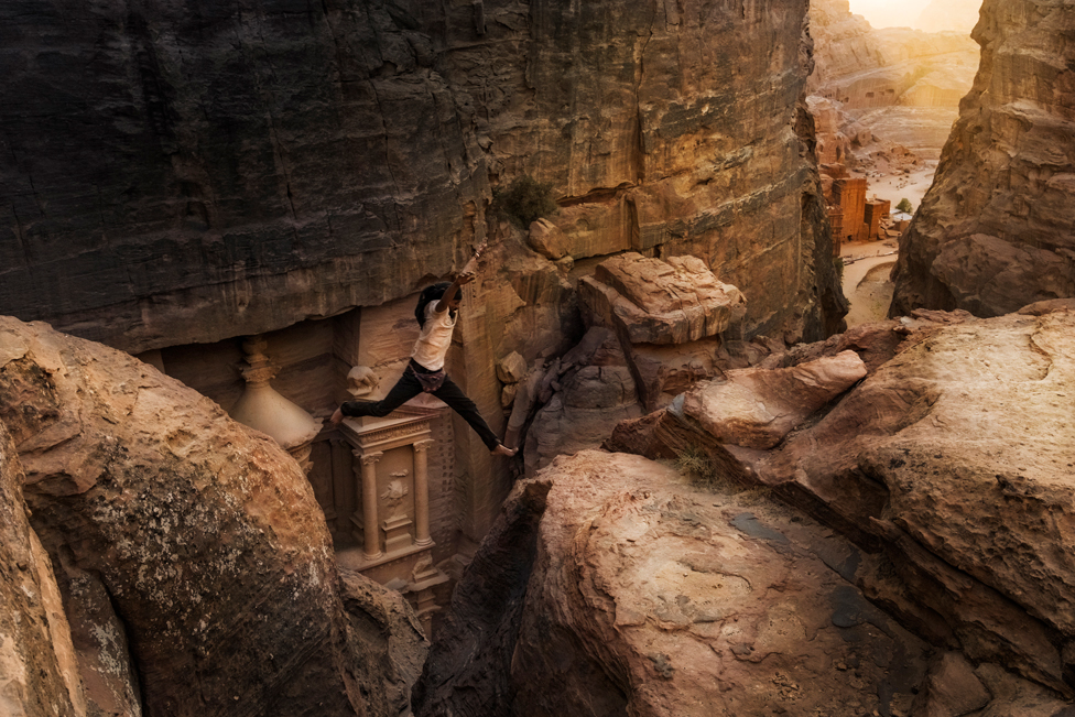 Beduin skače preko male klisure između stena u drevnoj Petri, Jordan.