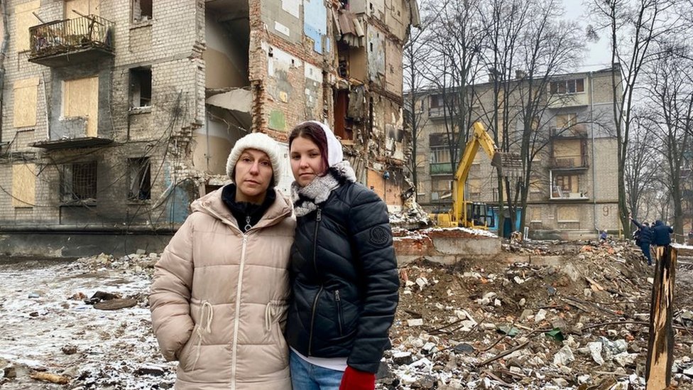 Maryna Ovcharenko and mother in front of damaged buildings
