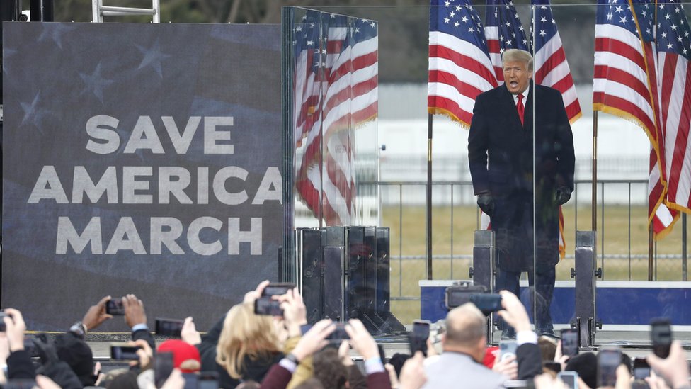 Amerika i politika: Vrhovni sud odlučuje da li Tramp može da se kandiduje za predsednika 2 Trump standing at microphone next to sign reading Save America March