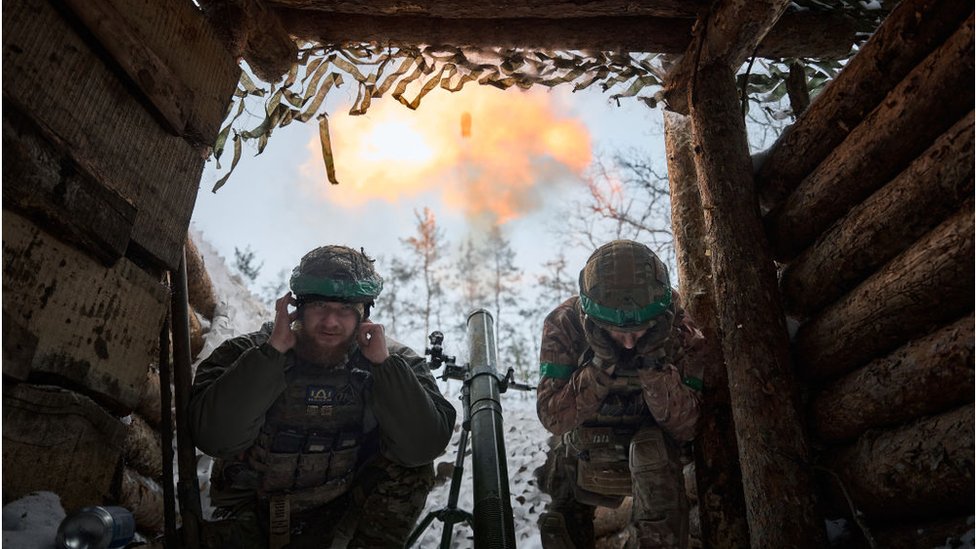 Two Ukrainian soldiers duck after firing a mortar
