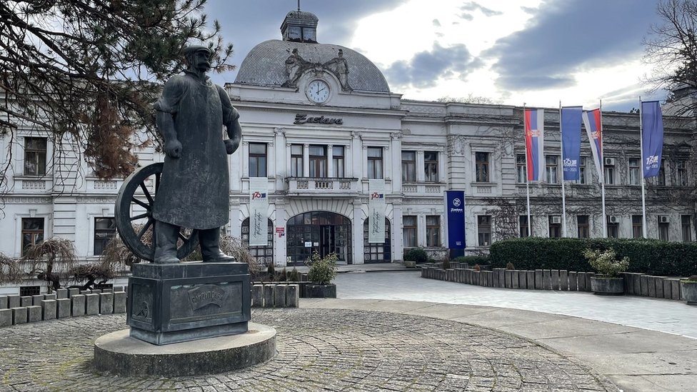 Spomenik Topolivcu ispred Upravne zgrade Zastave u Kragujevcu, na postamentu sadrži sliku radničkih demostracija od 27. februara 1876.