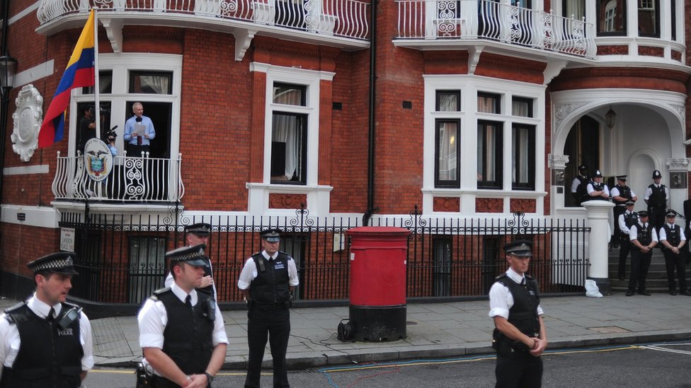 Džulijan Asanž i Vikiliks: Aktivista ili egzibicionista i hoće li biti izručen Americi 8 Police officers stand guard as Wikileaks founder Julian Assange addresses the media and his supporters from the balcony of the Ecuadorian Embassy in London, 19 August 2012