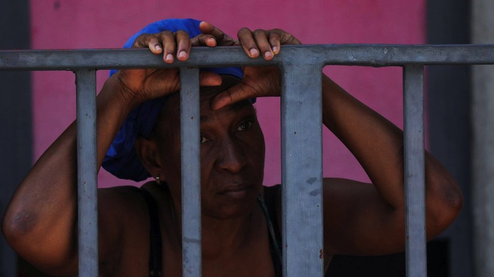 Žena tužno gleda napolje kroz rešetke metalne kapije oko školske zgrade