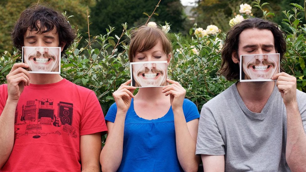 Two men and a woman hold up photographs of mouths in front of their faces