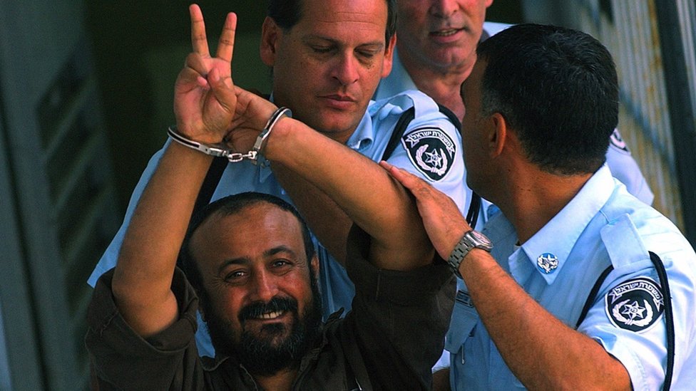 Handcuffed and flashing the 'V'-sign, Marwan Barghouti, the leader of Yasser Arafat's Fatah movement in the West Bank, is flanked by Israeli policemen as he is led to a police vehicle on 29 September 2003 on his way back to jail, after appearing before a Tel Aviv court
