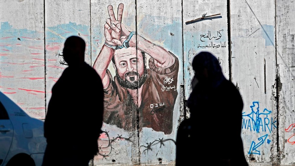 Palestinci prolaze pored grafita koji prikazuje palestinskog zatvorenika Marvana Bargutija na izraelskom kontroverznom zidu u Abu Disu, koji razdvaja grad na Zapadnoj obali Abu Dis od Jerusalima