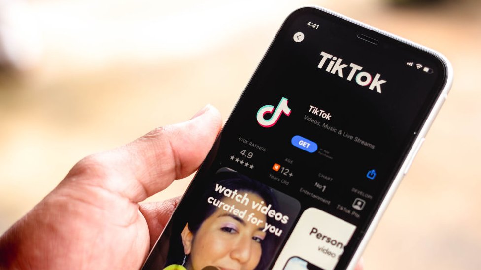 A woman holds a mobile showing TikTok in the the app store