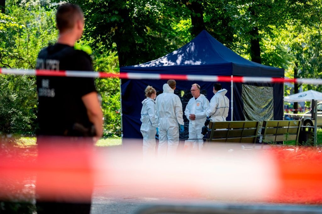 Police standing around a blue tent in a park over a dead body