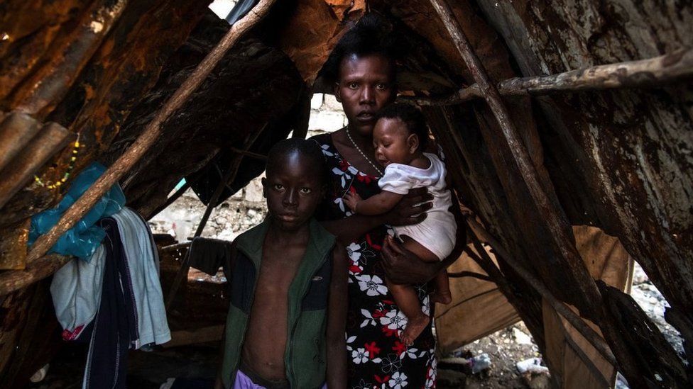 A Haitian woman with two children in a hut