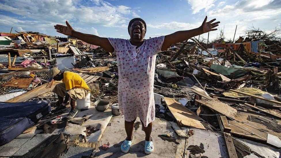 A woman holds her arms aloft in despair among the wreckage caused by a hurricane