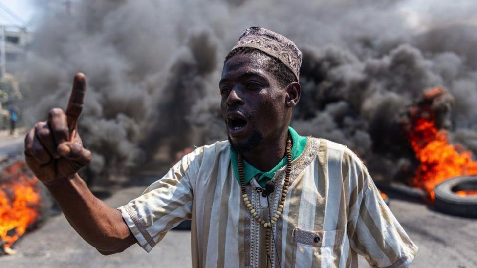 Nasilje na Haitiju: Šta je pošlo po zlu - pet istorijskih činilaca koji su uzrokovali neprolaznu krizu u zemlji 1 A man stands in front of an enormous plume of smoke as tyres burn