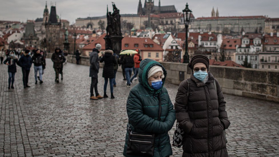 Two women walk side by side in Prague wearing face masks