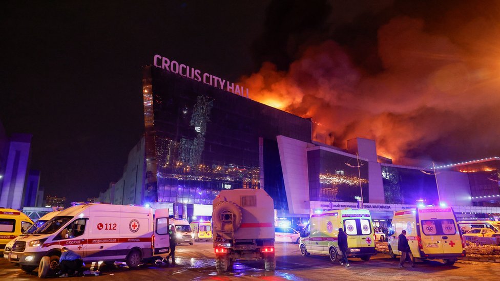 Vehicles of Russian emergency services are parked near the burning Crocus City Hall concert