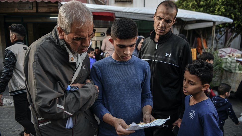 Dva muškarca i dva dečaka na ulici u Gazi čitaju letak sa upozorenjima izraelske vojske za evakuaciju