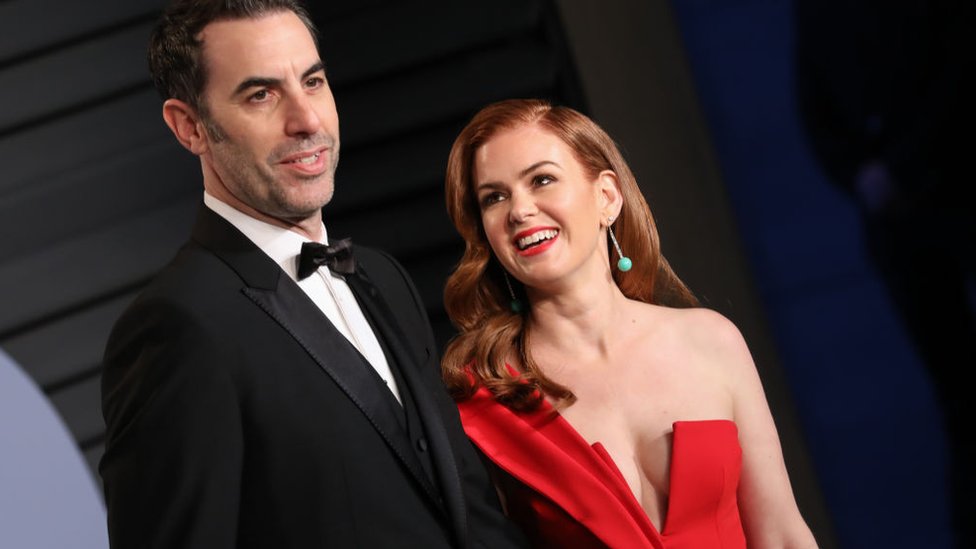 Sacha Baron Cohen in a tuxedo and Isla Fisher in a red dress